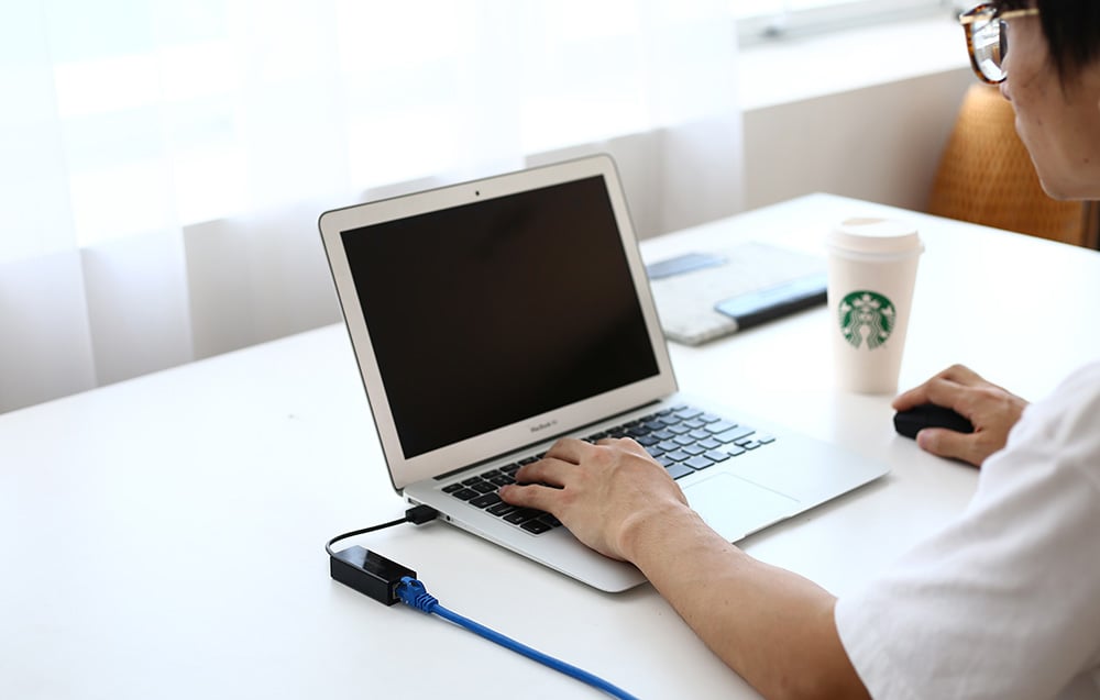 A person working on a laptop in a café, next to a Starbucks cup and a network adapter with a blue cable