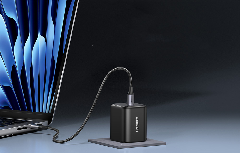 Black UGREEN charger with a flexible cable connected to a MacBook on a dark gray background