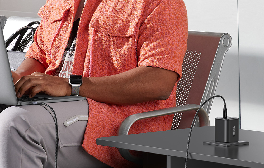 Woman in an orange sweater working on a laptop in an airplane with the UGREEN charger on the table