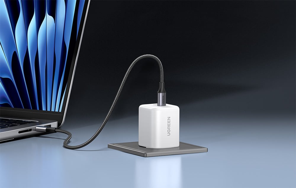 White UGREEN charger with a flexible cable connected to a MacBook on a dark gray background