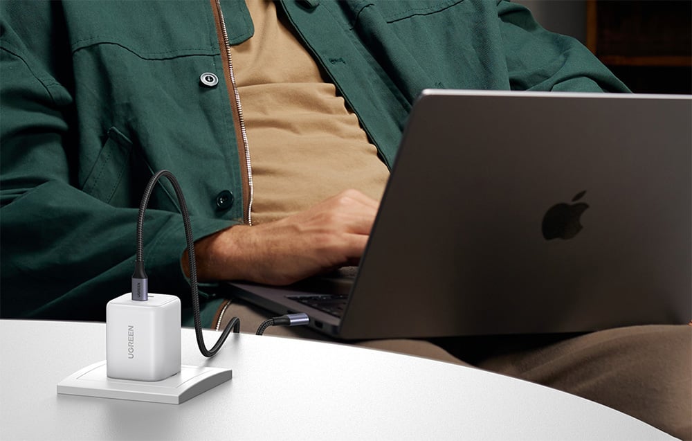 Man in a green jacket working on a laptop with the UGREEN charger connected on a white desk
