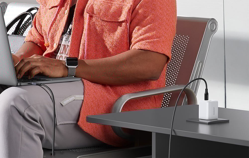 Woman in an orange sweater working on a laptop in an airplane with the UGREEN charger on the table