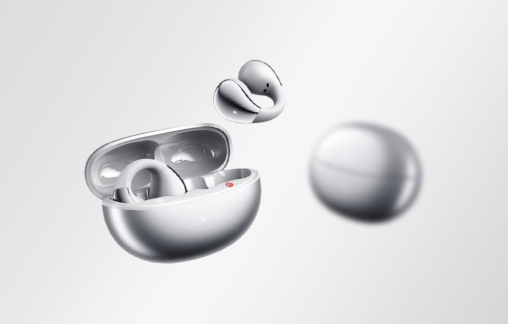 Etui QCY z otwartą pokrywką i jedną unoszącą się słuchawką, obok rozmazanego etui w tle