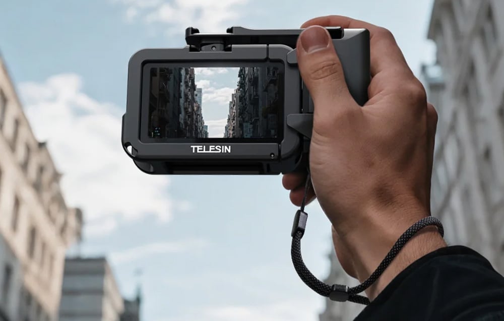 Ręka trzyma kamerę DJI w obudowie Telesin filmującą miejską ulicę z budynkami