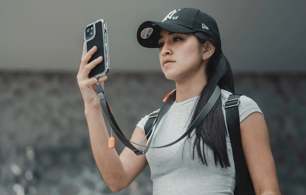 A woman wearing a cap using a phone mounted to a gray neck strap