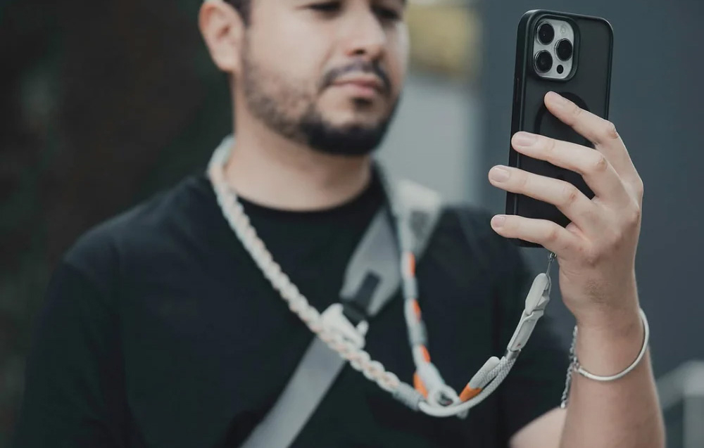 A man in a black shirt using a smartphone attached to a PGYTECH neck strap