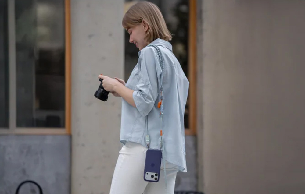 Short-haired woman holding a camera, with the PGYTECH strap and smartphone hanging from her shoulder