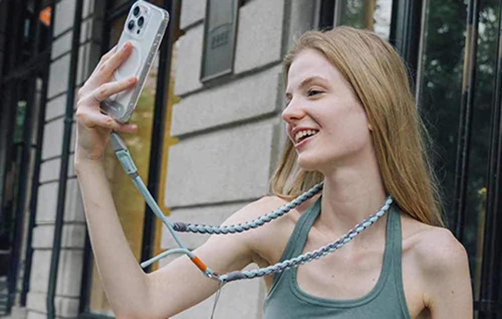 Blonde woman taking a selfie with her smartphone attached to the PGYTECH strap