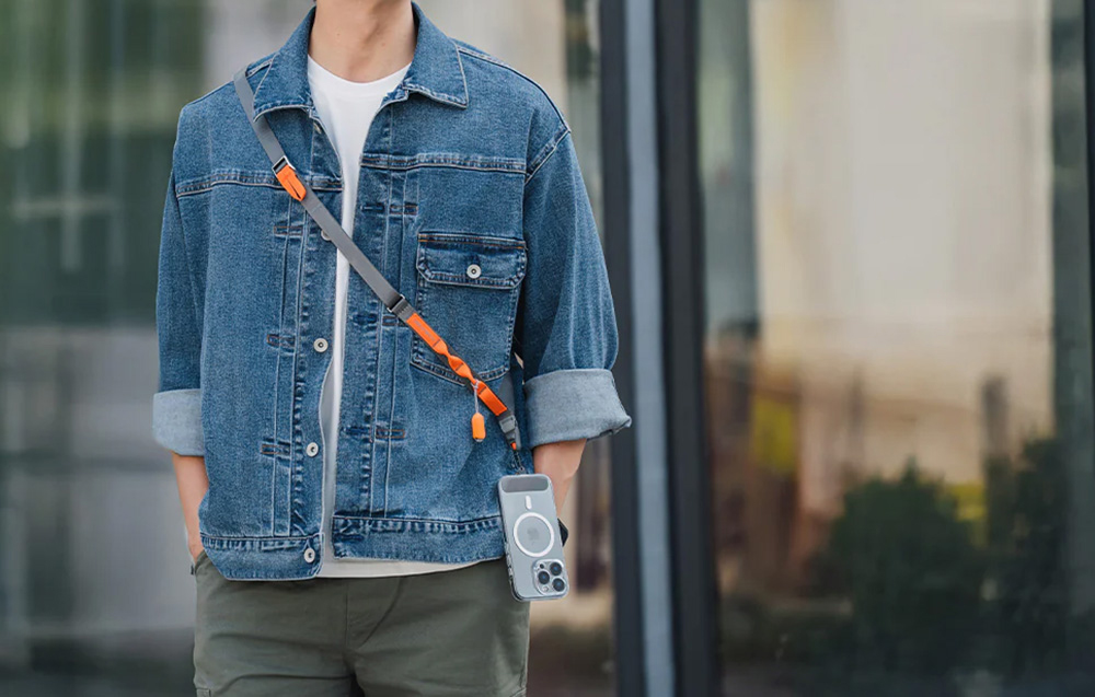 A man wearing a denim jacket and PGYTECH neck strap, to which a smartphone is attached