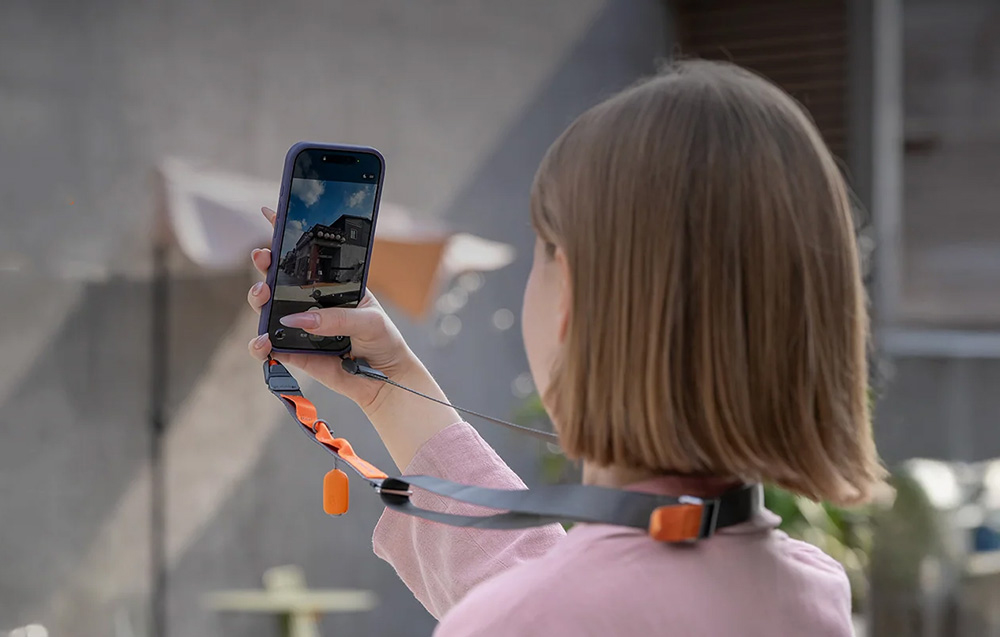 A woman photographing a building with her smartphone attached to the PGYTECH neck strap