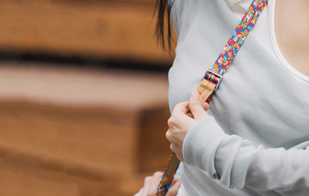 A woman in a light t-shirt adjusts the length of the PGYTECH strap, which is hanging over her shoulder