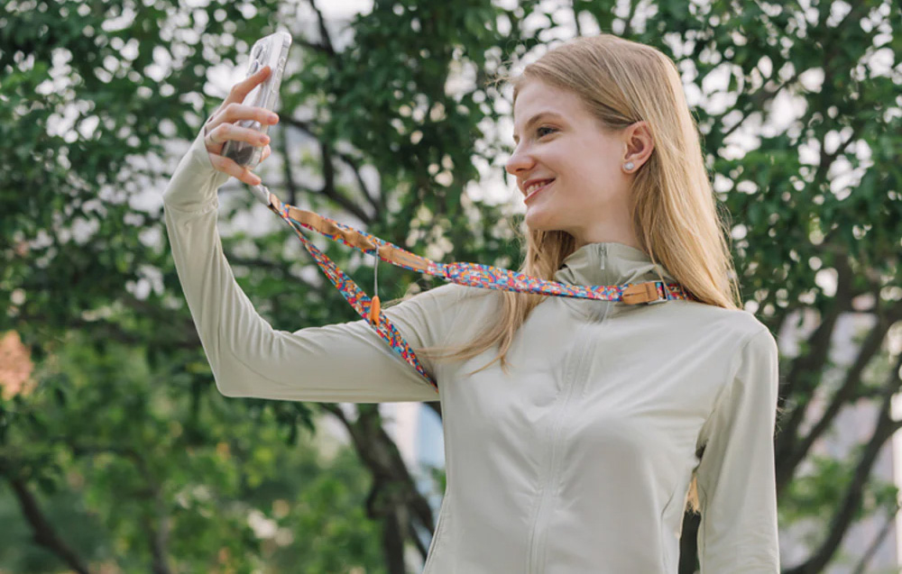 A young woman takes a selfie with a smartphone mounted to the PGYTECH strap hanging around her neck