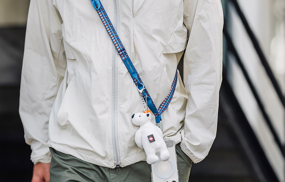 A person in a white jacket wearing the PGYTECH strap around their neck, with a smartphone and accessories attached