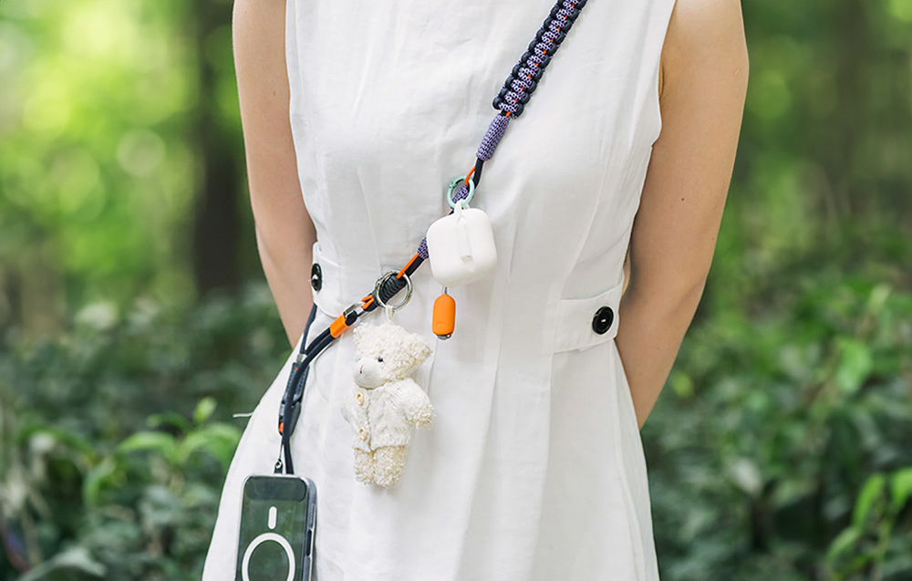 A woman in a white dress is wearing a PGYTECH strap with a smartphone and accessories attached