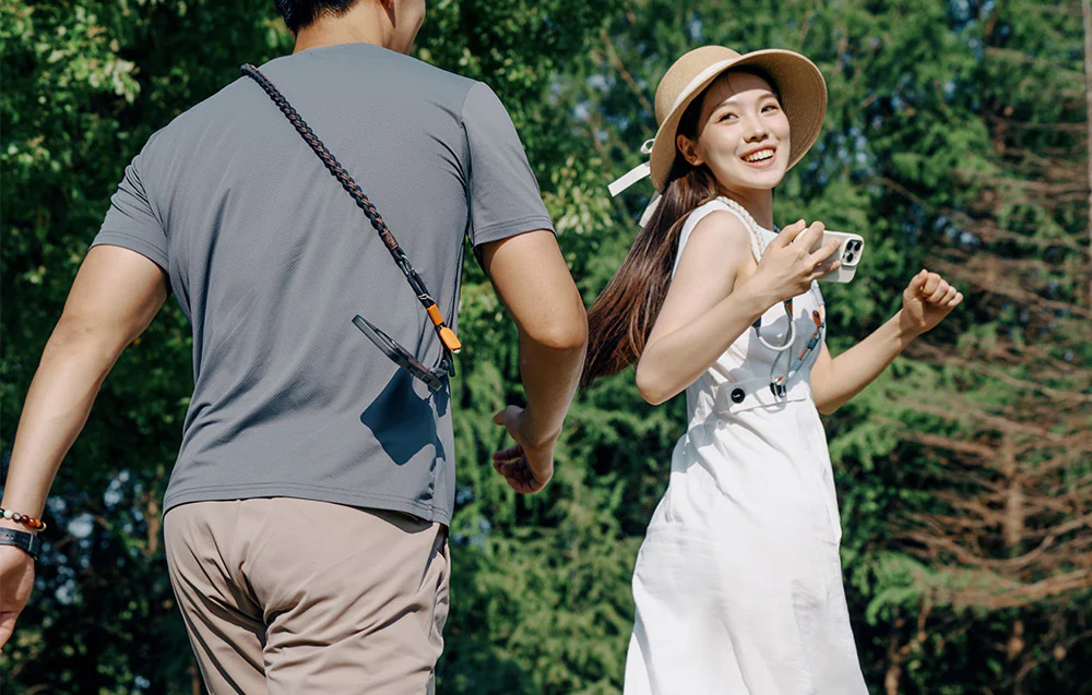 A man walking behind a woman in a white dress and hat, both wearing PGYTECH straps