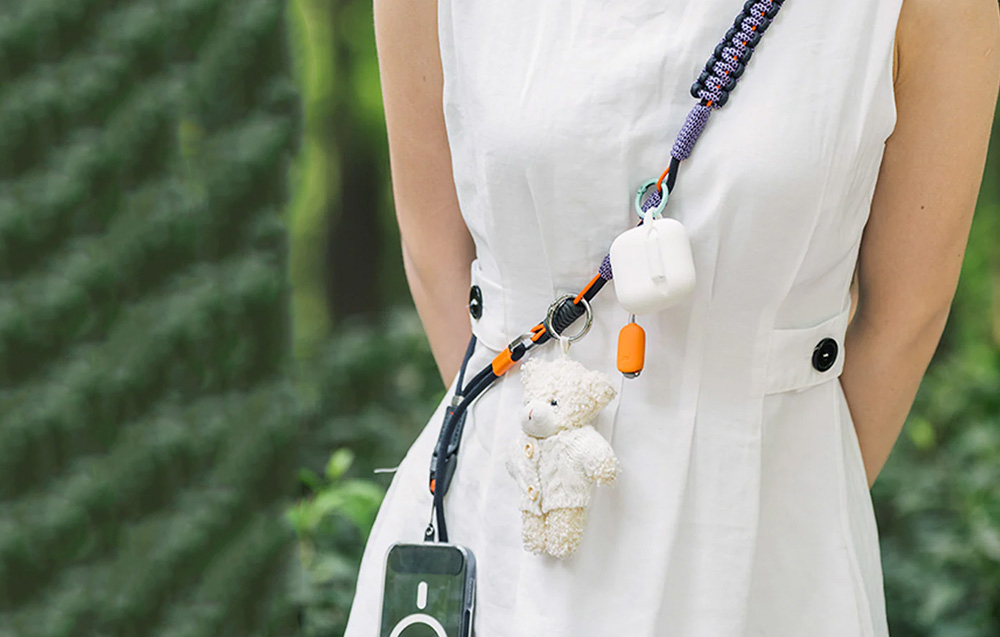A woman in a white dress wears the strap hanging on her shoulder, to which accessories and a smartphone are attached