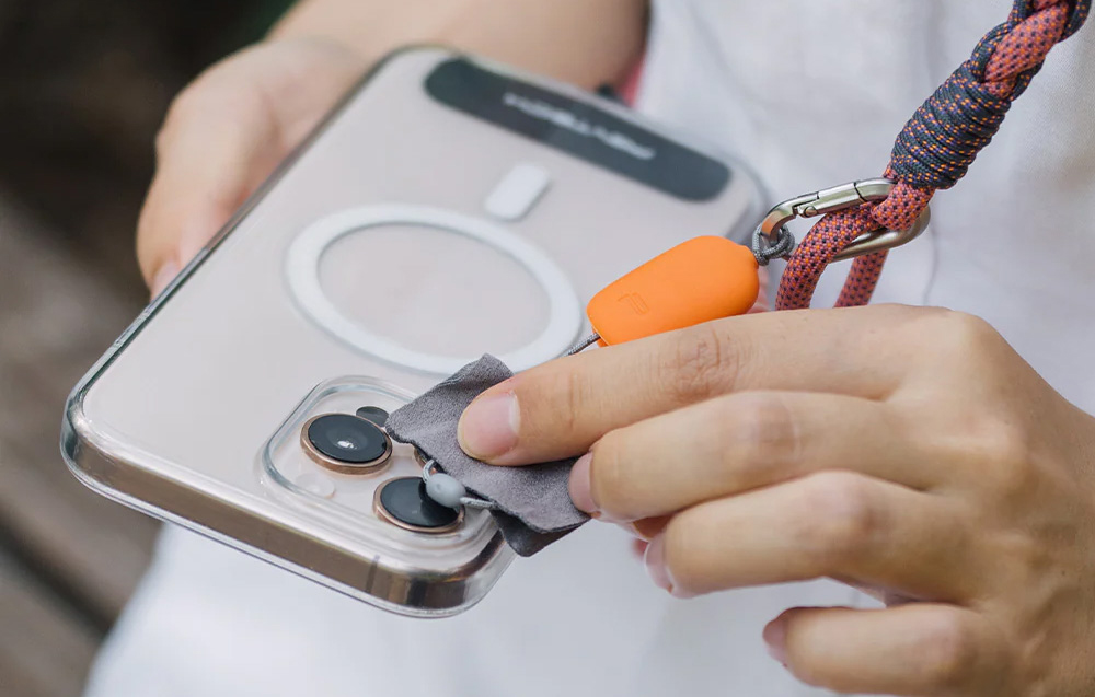 A person cleaning the lens of their smartphone with the orange cloth built into the PGYTECH strap