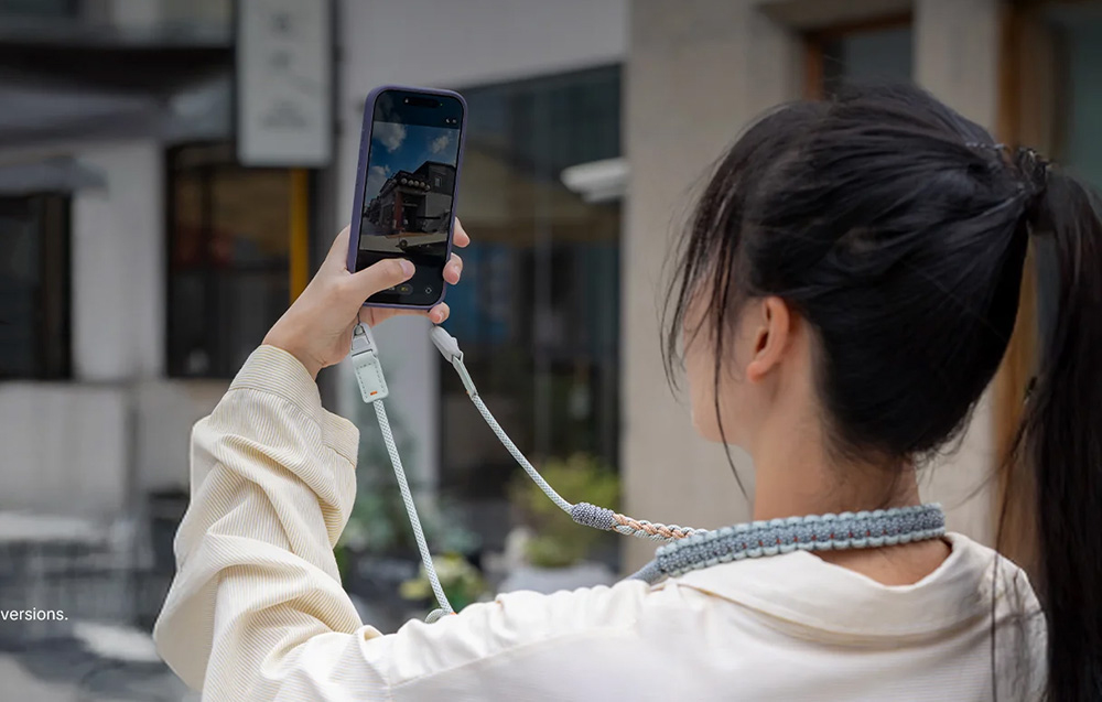 A woman with black hair photographs a building with a smartphone attached to the PGYTECH strap