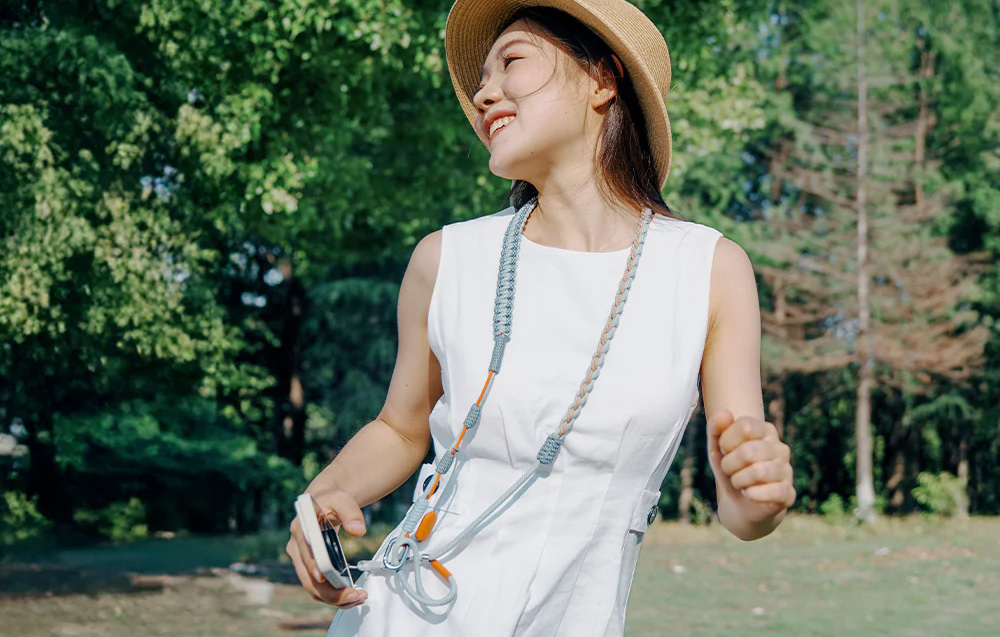 A woman in a white dress and hat wears the PGYTECH strap around her neck