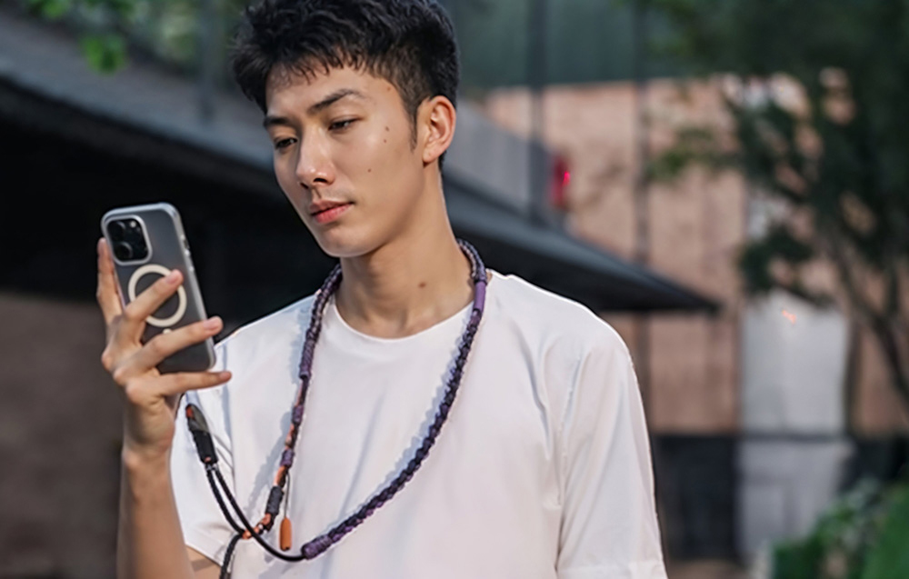 A man in a white t-shirt using his smartphone while wearing the PGYTECH strap around his neck