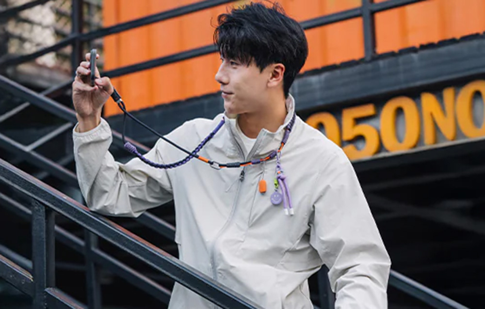 A man in a white jacket leaning against stairs taking a photo with his smartphone mounted to the PGYTECH strap