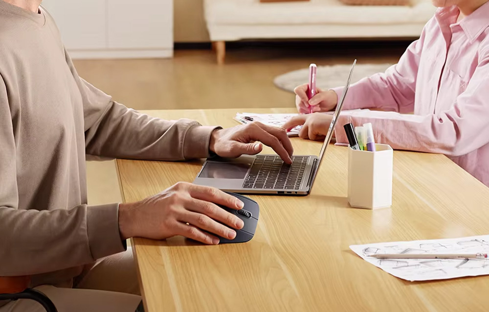 Mężczyzna pracujący przy laptopie, naprzeciwko siedzi dziewczynka i maluje w zeszycie