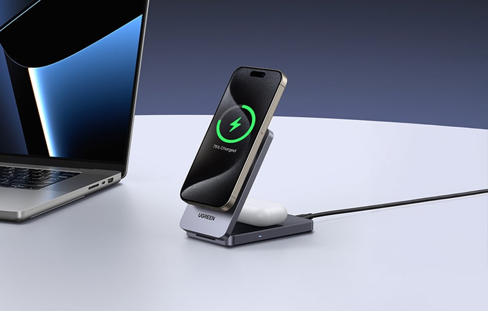 Słuchawki TWS i smartfon podłączone do ładowarki magnetycznej, obok na stole laptop