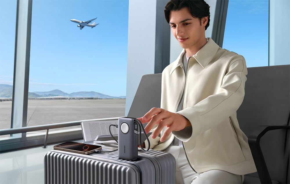 Mann sitzt am Flughafen, der Powerbank ist an ein Smartphone angeschlossen und auf einem Koffer platziert