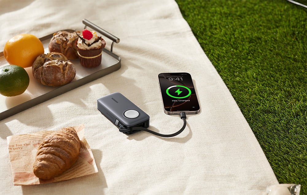 Powerbank, die mit einem Smartphone auf einer Picknickdecke verbunden ist, daneben ein Tablett mit Essen
