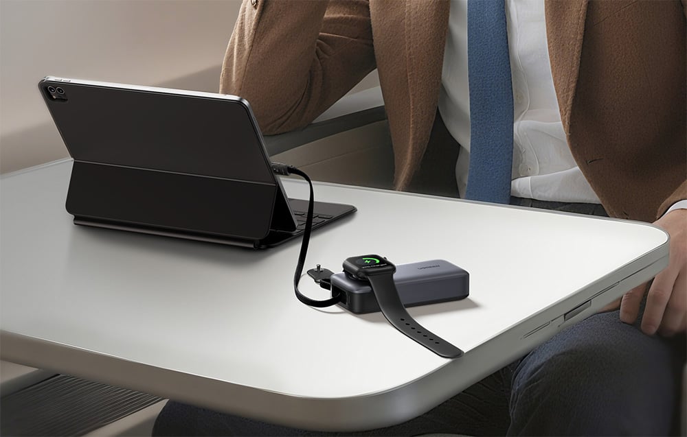 Mann sitzt an einem Tisch mit einem Tablet, das mit dem Powerbank und einer Smartwatch verbunden ist