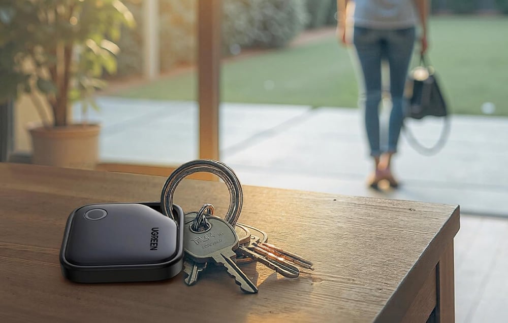 Klucze z lokalizatorem na drewnianej szafce. W oddali kobieta wychodząca z domu