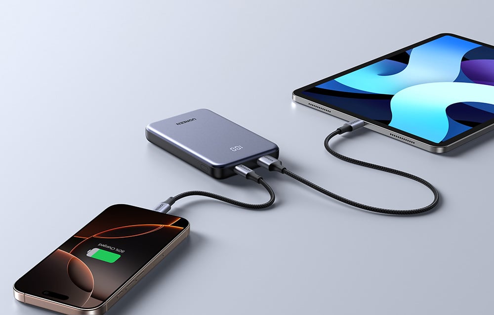 Grauer Ugreen-Powerbank auf einem Tisch, verbunden mit einem Laptop und einem Tablet