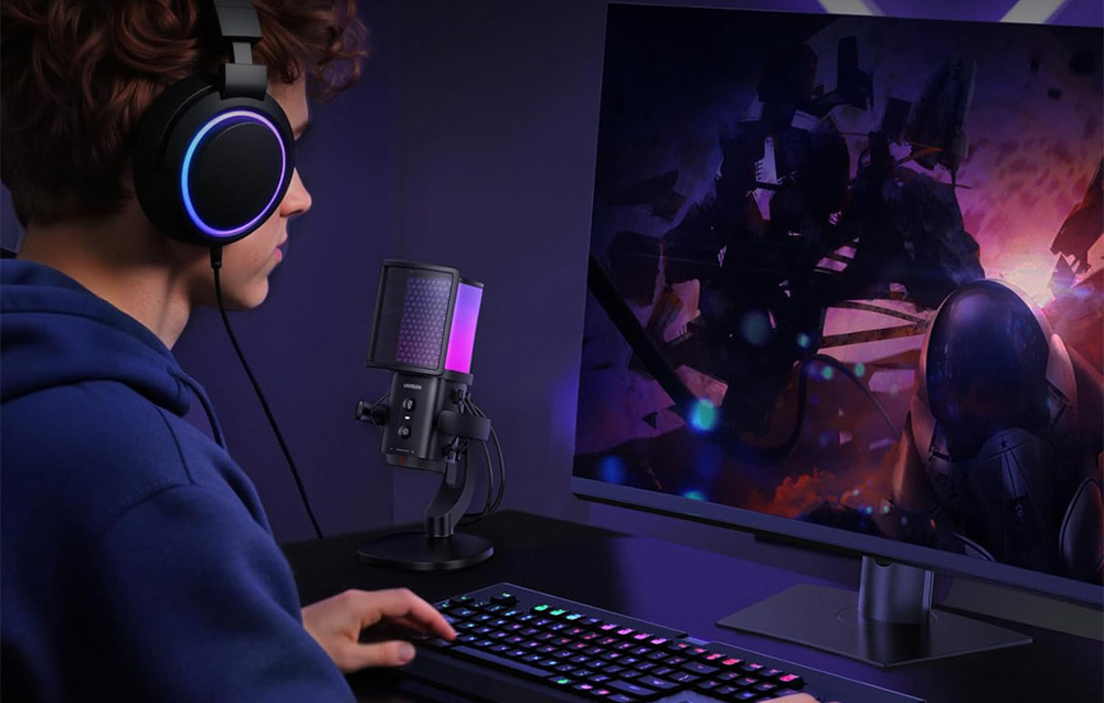 Chłopak w słuchawkach gra w grę komputerową, na biurku obok stoi mikrofon