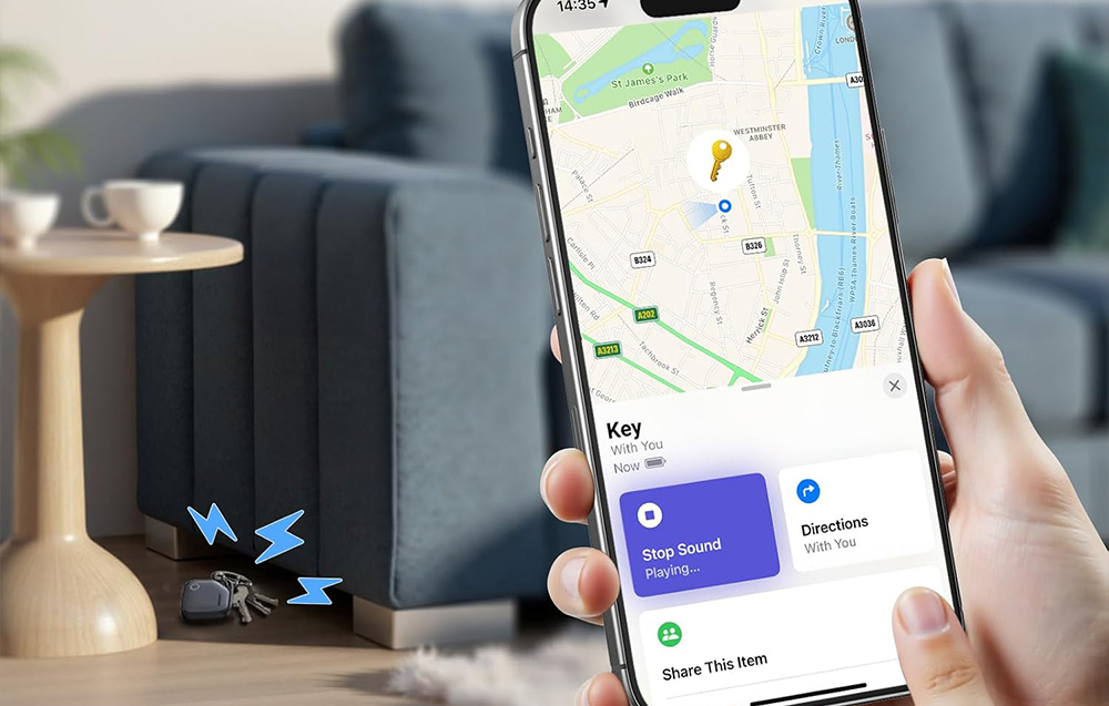 Trzymany w dłoni smartfon, w tle leżące na podłodze klucze z lokalizatorem