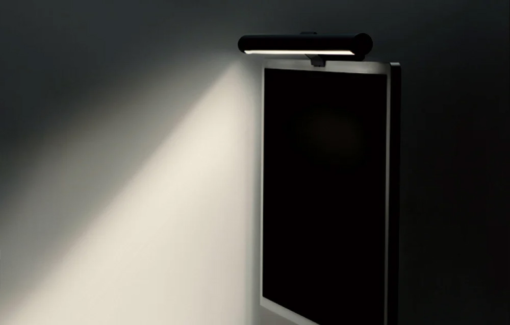 Lampa biurkowa typu light bar zamontowana na górnej krawędzi monitora, oświetlająca ścianę pod kątem