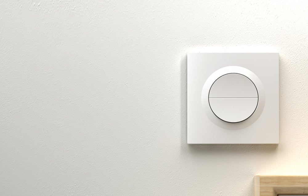 Biały przełącznik ścienny z okrągłym przyciskiem podzielonym na dwie strefy, zamontowany na jasnej ścianie