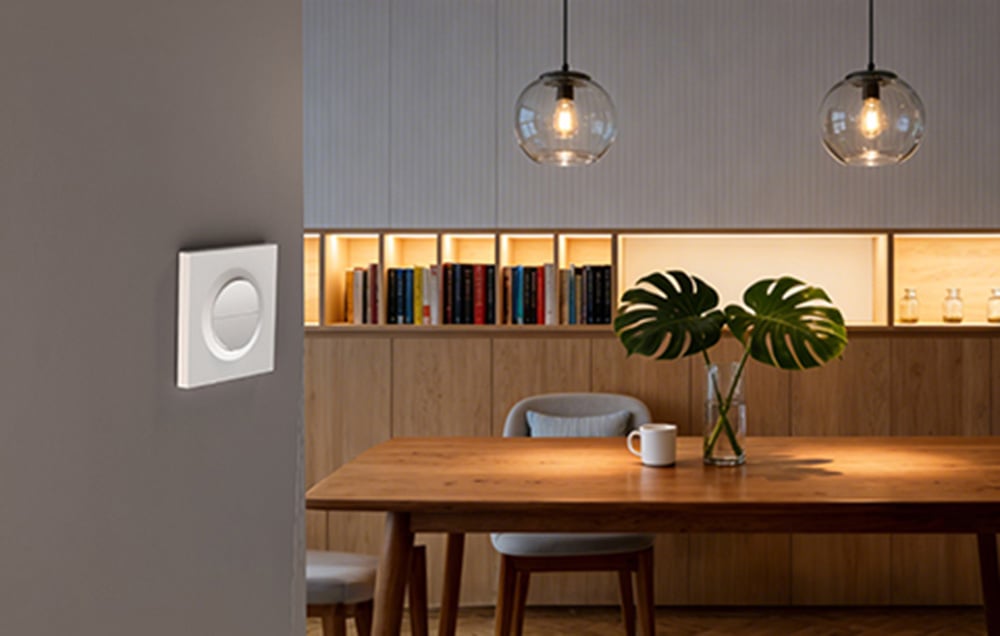 Elegancki biały przełącznik ścienny SONOFF w nowoczesnej jadalni z drewnianym stołem, oświetleniem wiszącym i podświetlaną biblioteczką