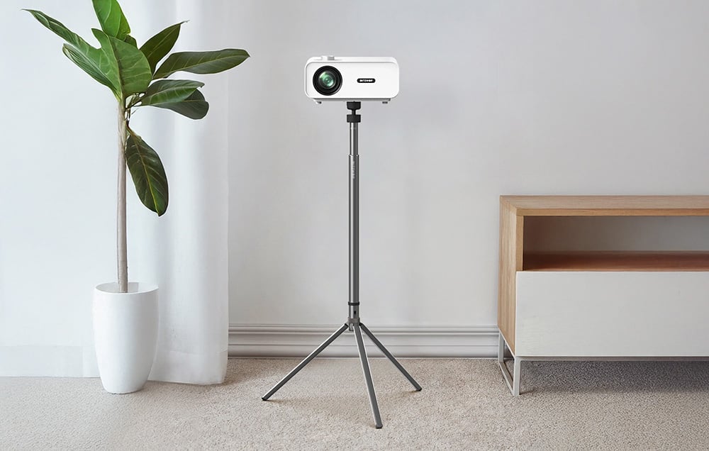 Projektor ustawiony na statywie w minimalistycznym wnętrzu z rośliną doniczkową i niską szafką.