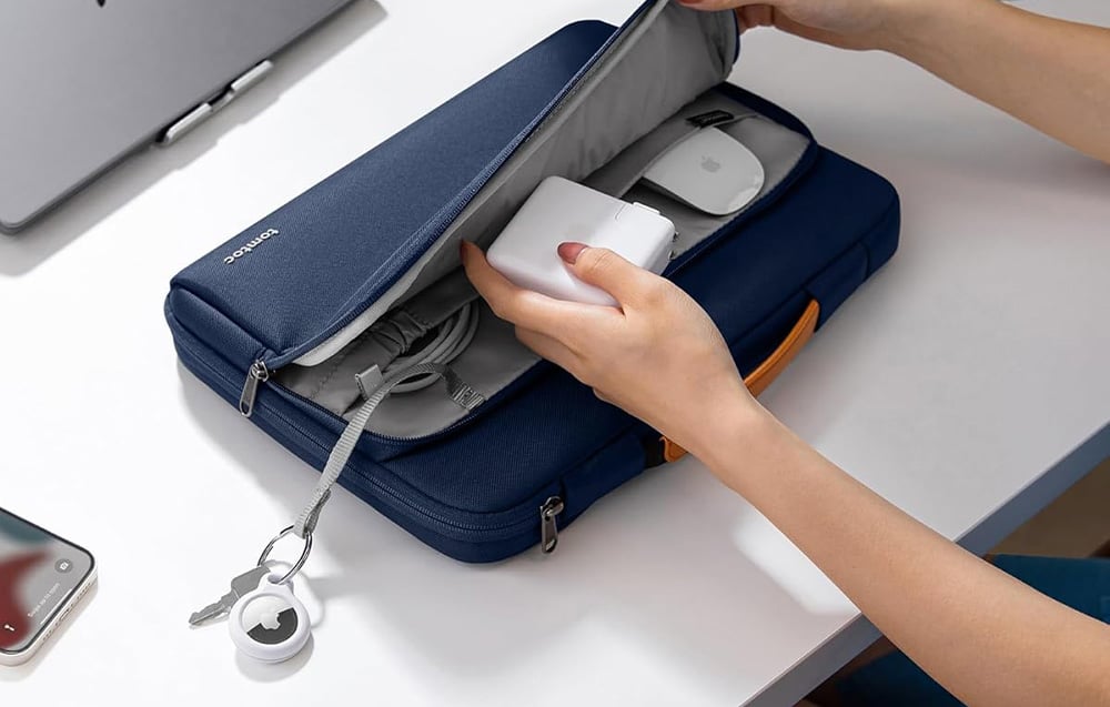 A woman packing a power charger into a laptop bag.