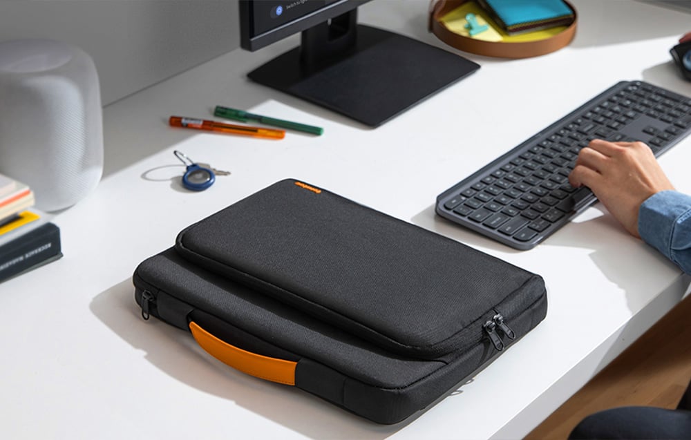 Black laptop bag with orange handle on a desk next to a man working at a computer