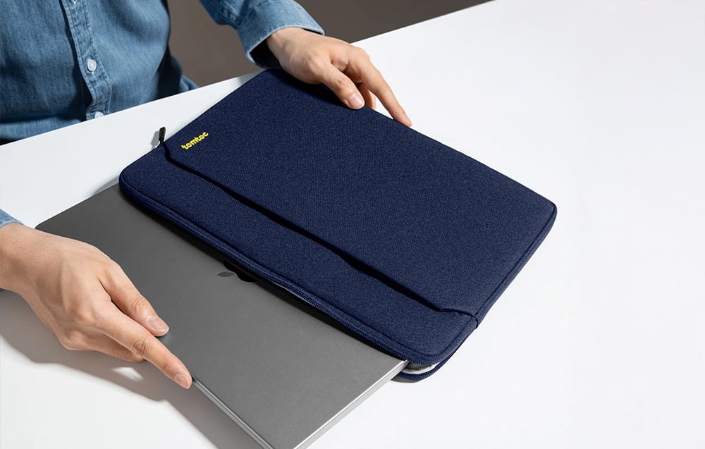 A woman putting a laptop into a navy tomtoc bag