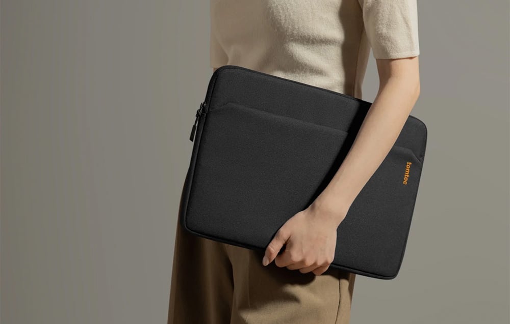 A woman in light clothing holding a black tomtoc laptop sleeve