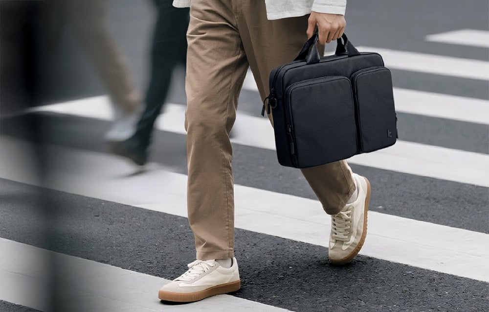 Mężczyzna przechodzi przez przejście dla pieszych trzymając w dłoni czarną torbę na laptopa