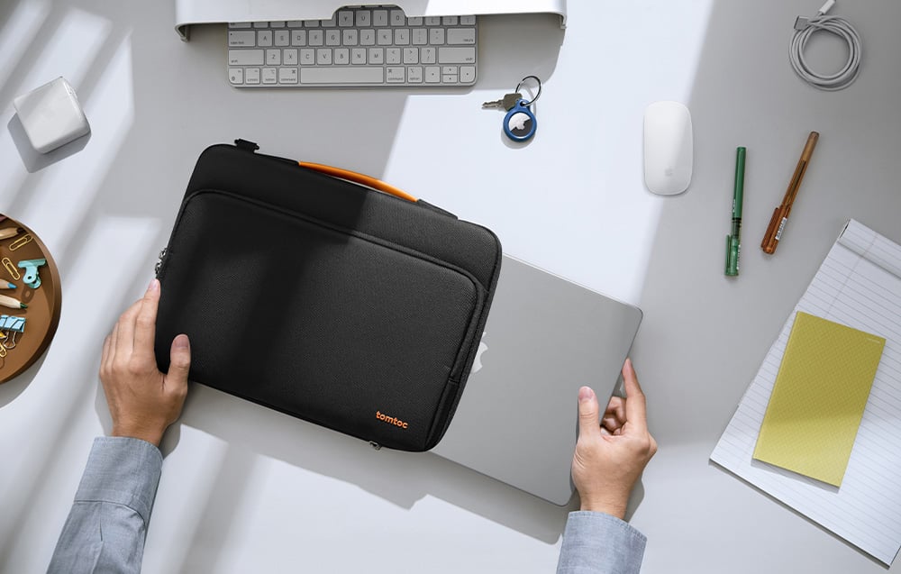 Laptop being taken out of a black tomtoc bag on a desk next to a keyboard and other small items