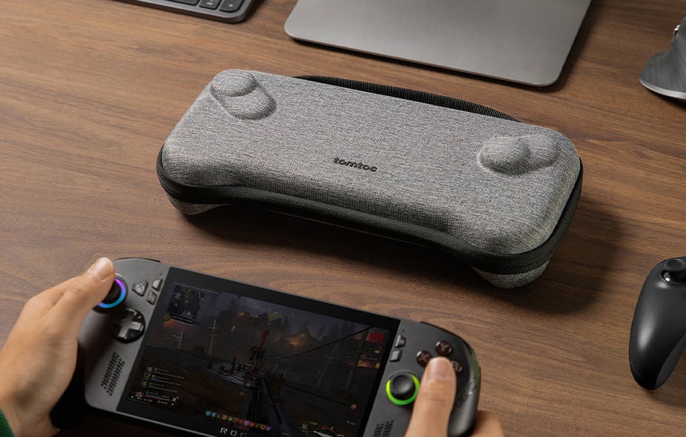 Console held in hand, next to the gray tomtoc case on a desk