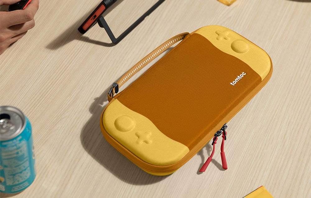 Żółte etui tomtoc na konsolę na jasnym stoliku obok puszki z napojem i smartfona