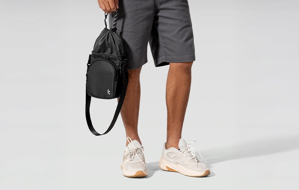 Mann in dunklen Shorts und hellen Schuhen hält eine schwarze Tasche in der Hand