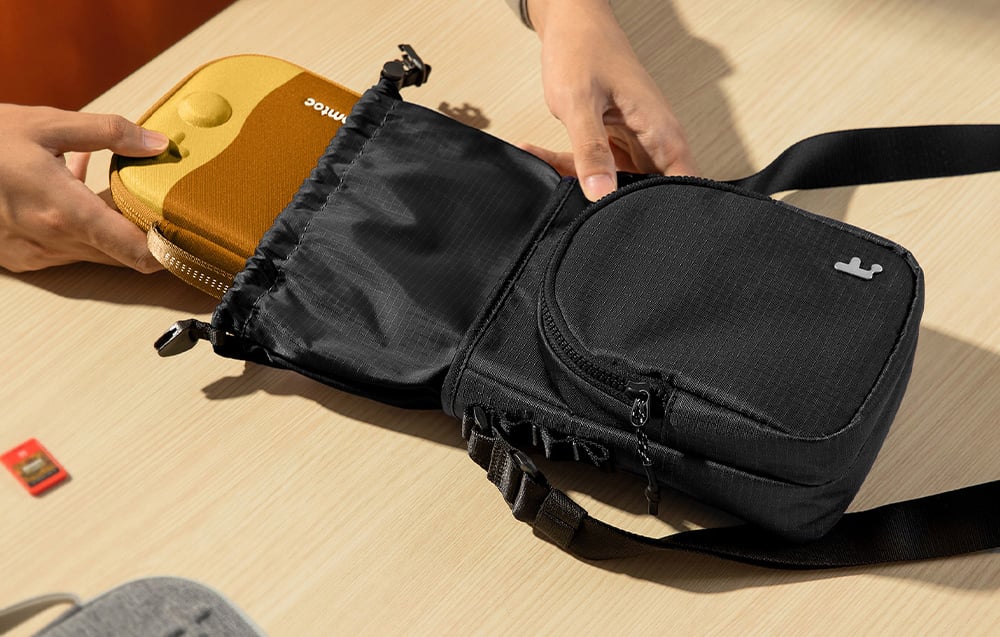 Nintendo Switch Konsole in einer Hülle wird in eine schwarze Tasche gelegt, die auf einem Tisch liegt