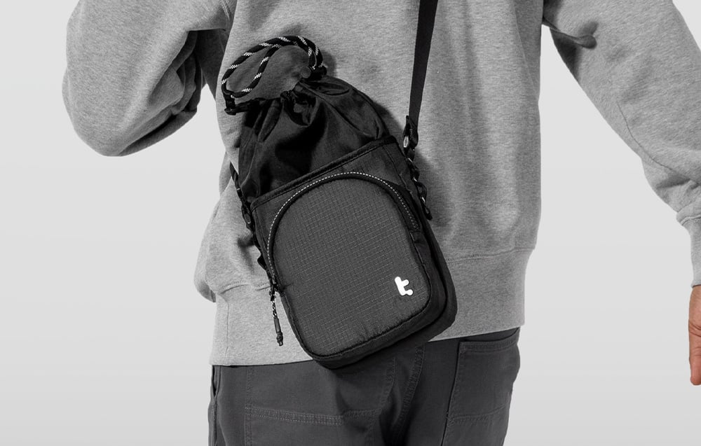 Mann in grauem Sweatshirt und schwarzen Hosen mit über der Schulter hängender Tasche