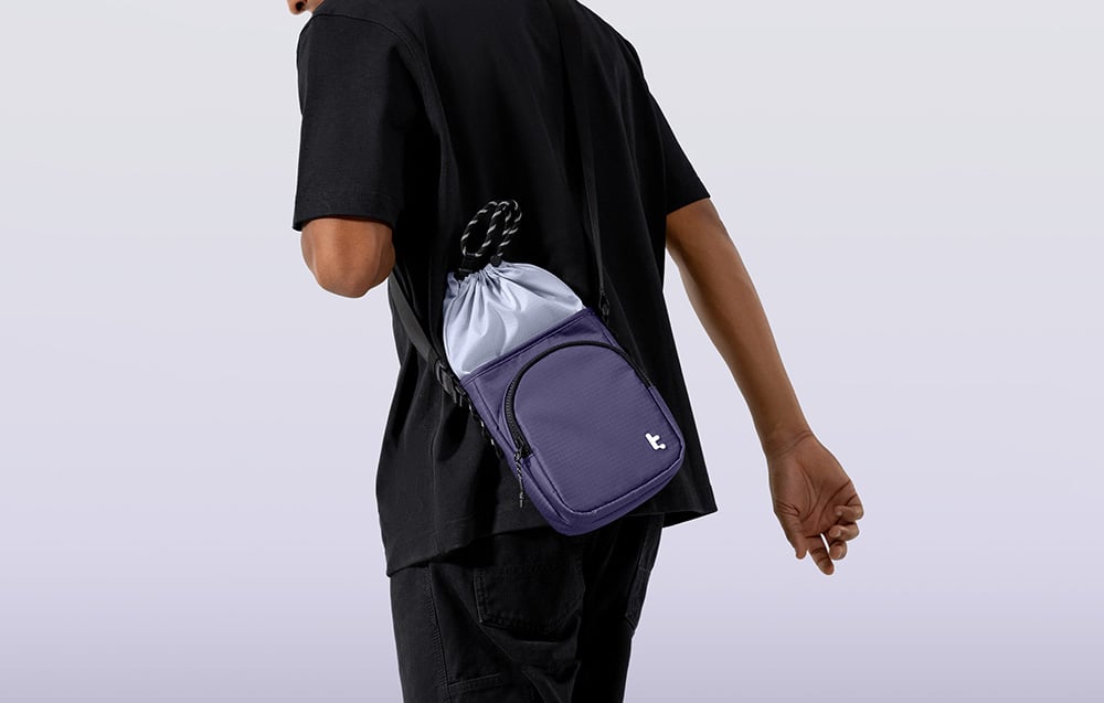 A man in a black shirt and black pants with a purple bag slung over his shoulder
